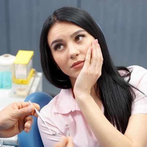 Woman holding cheek in pain before emergency dentistry