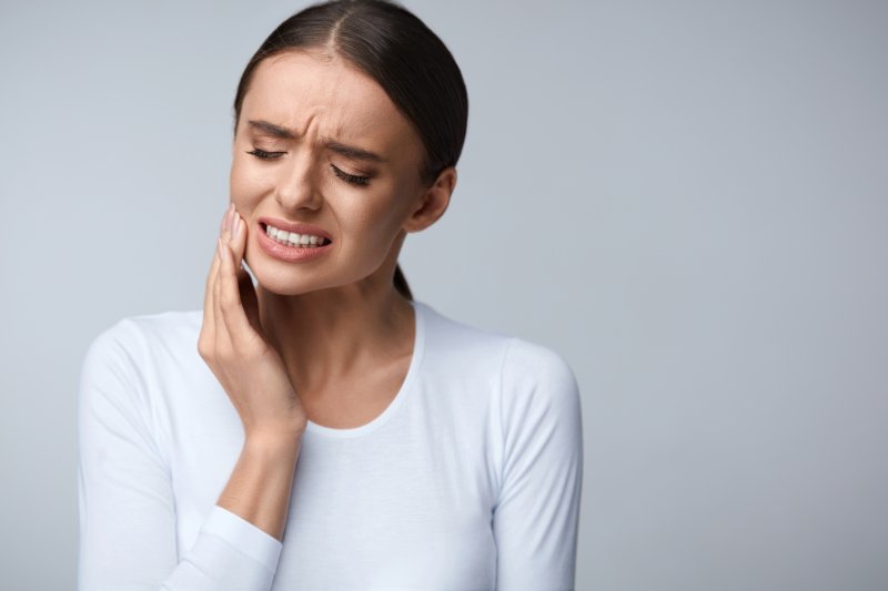 person with toothache who needs emergency dental visit holding cheek