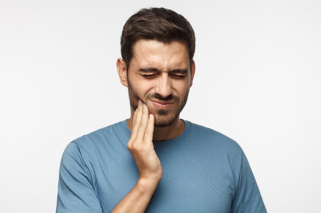 person holding cheek before wisdom tooth extraction