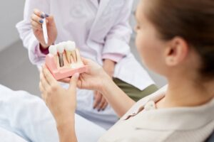 Young woman holding dental implant model with dentist pointing to it. 